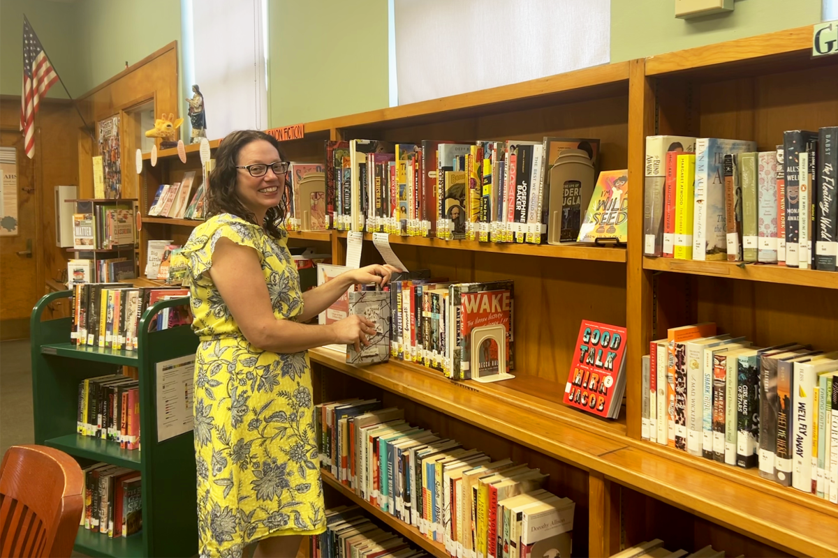 Librarian+Mrs.+Eisenstein+poses+with+her+display+of+BookTok+recommendations.+